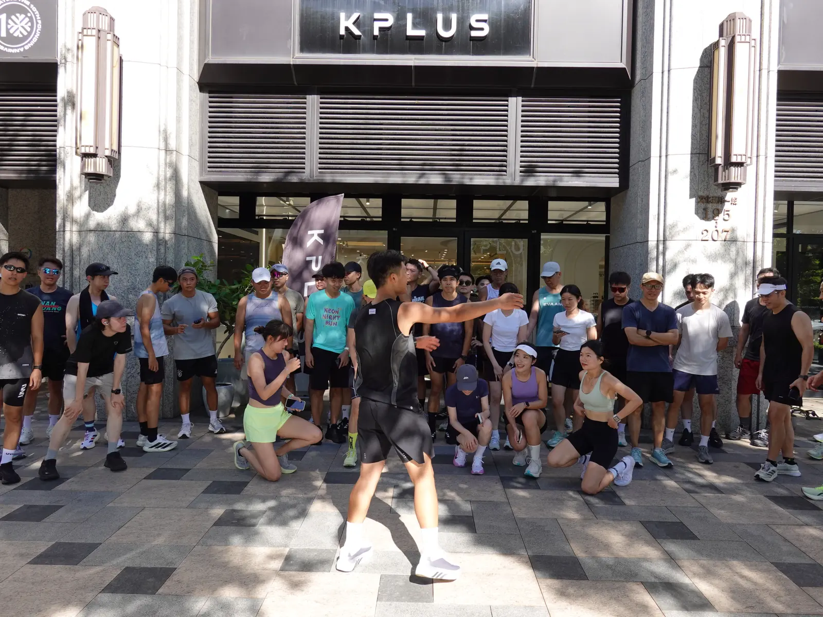 KPLUS 林口門市前，帶暖身的人伸手示範，參加者圍成半圈跟著做